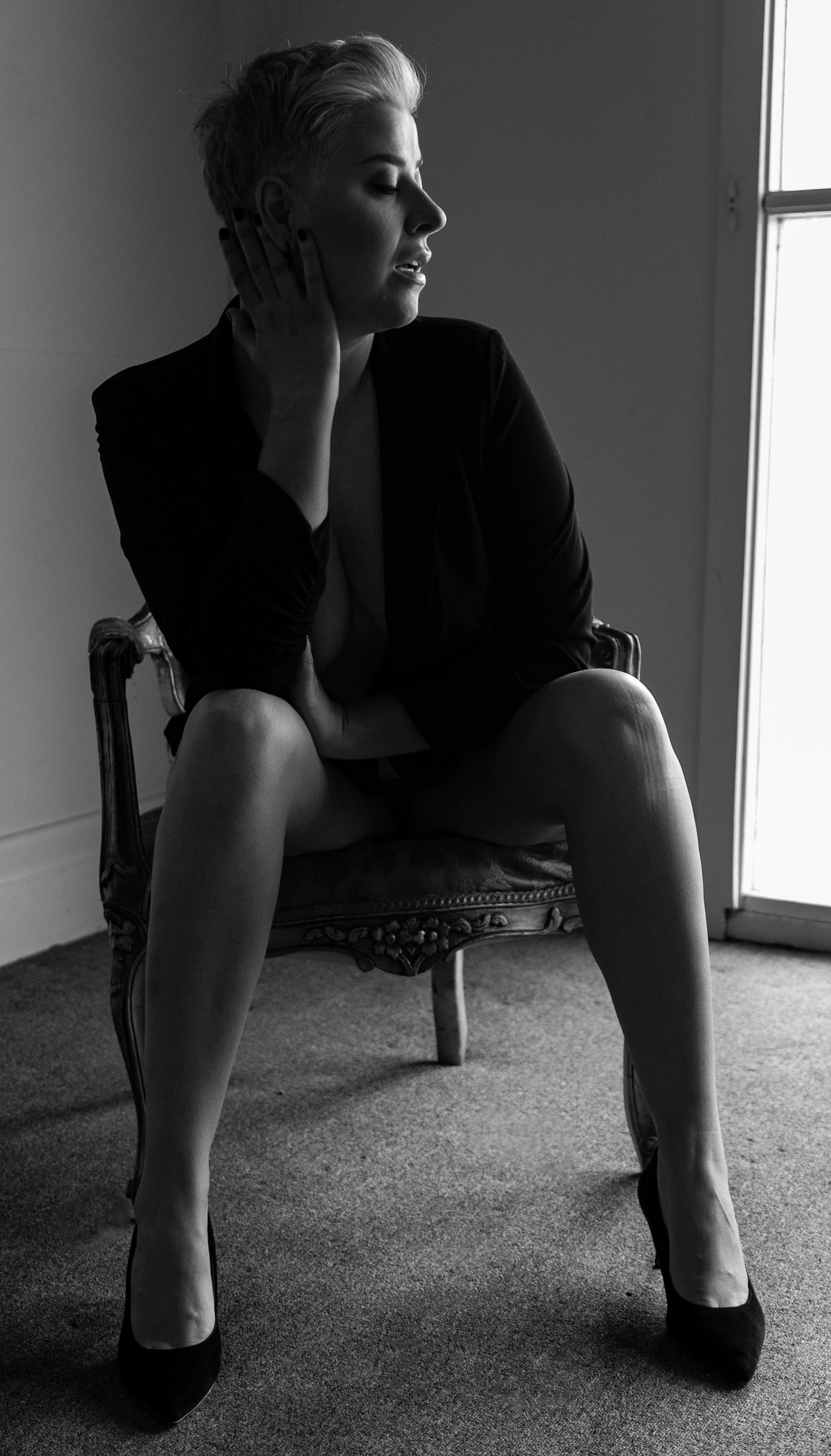 mature age female sitting on chair, black heels, black and white photo